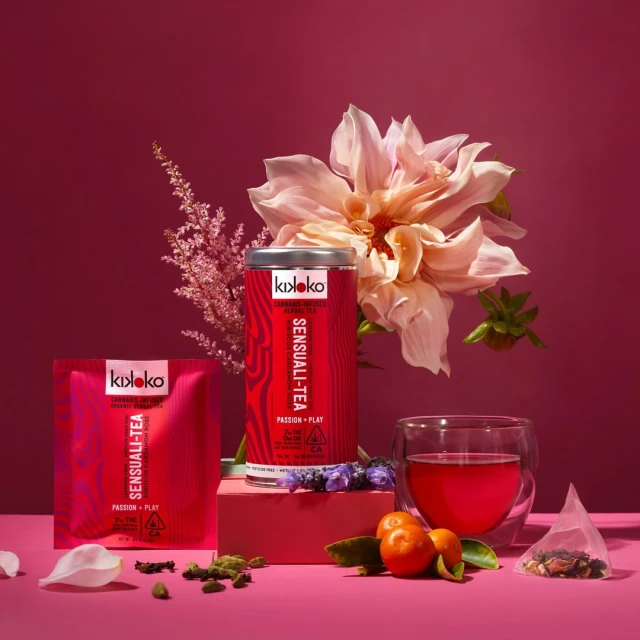 Kikoko Sensuali-Tea products on pink background with pink flowers, a clear tea cup, and loose tea; eye-level, medium shot.