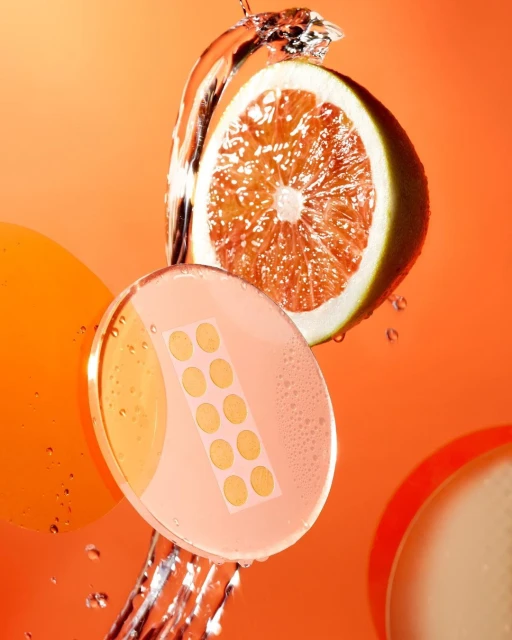 Citrus fruit slice with skin care patch and water splash against bright orange background in a studio setting.