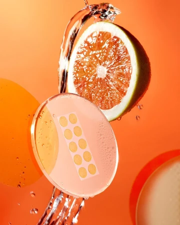 Citrus fruit slice with skin care patch and water splash against bright orange background in a studio setting.