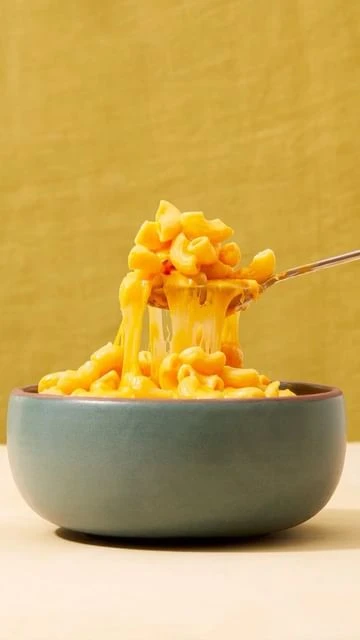 Bowl of macaroni and cheese with a fork lifting some of the cheesy pasta against a yellow background. Food and drink photography.