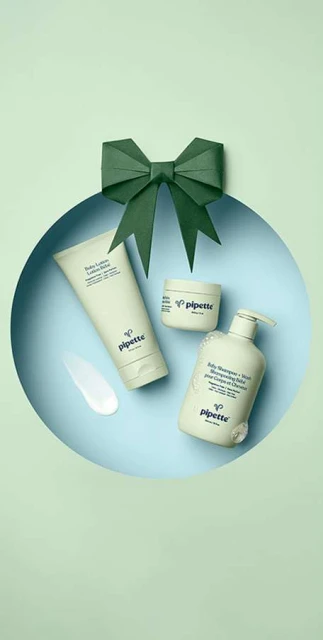 Baby bath and skincare products by Pipette are arranged around a green paper bow on a light blue and green backdrop.