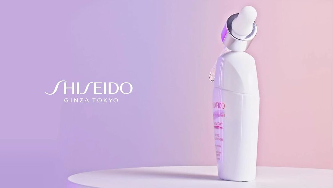 Shiseido Ginza Tokyo skincare product bottle on a white table, with a dropper applicator and a soft purple gradient background.