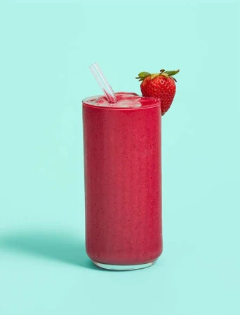 Eye-level shot of a tall glass filled with a vibrant red smoothie, garnished with a fresh strawberry and a clear straw against teal background.