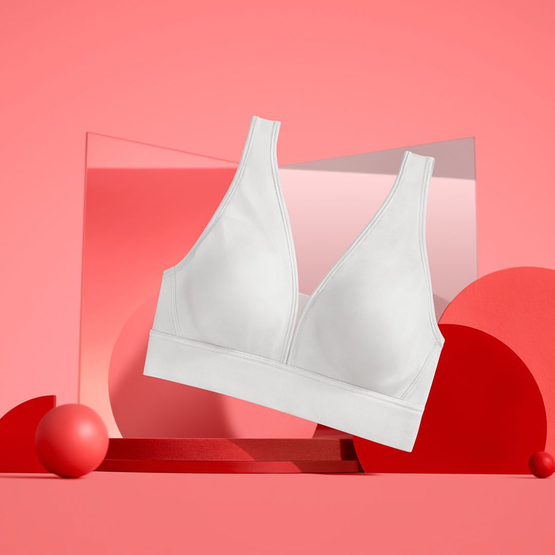 White bra floats against a pink geometric backdrop with red sphere accents, showcasing modern lingerie design in a studio setting.