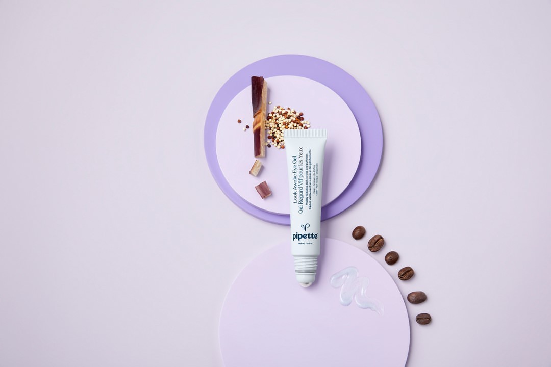 Eye gel tube by Pipette, brown coffee beans, and geometric lavender shapes on a pale lavender backdrop in studio product shot.