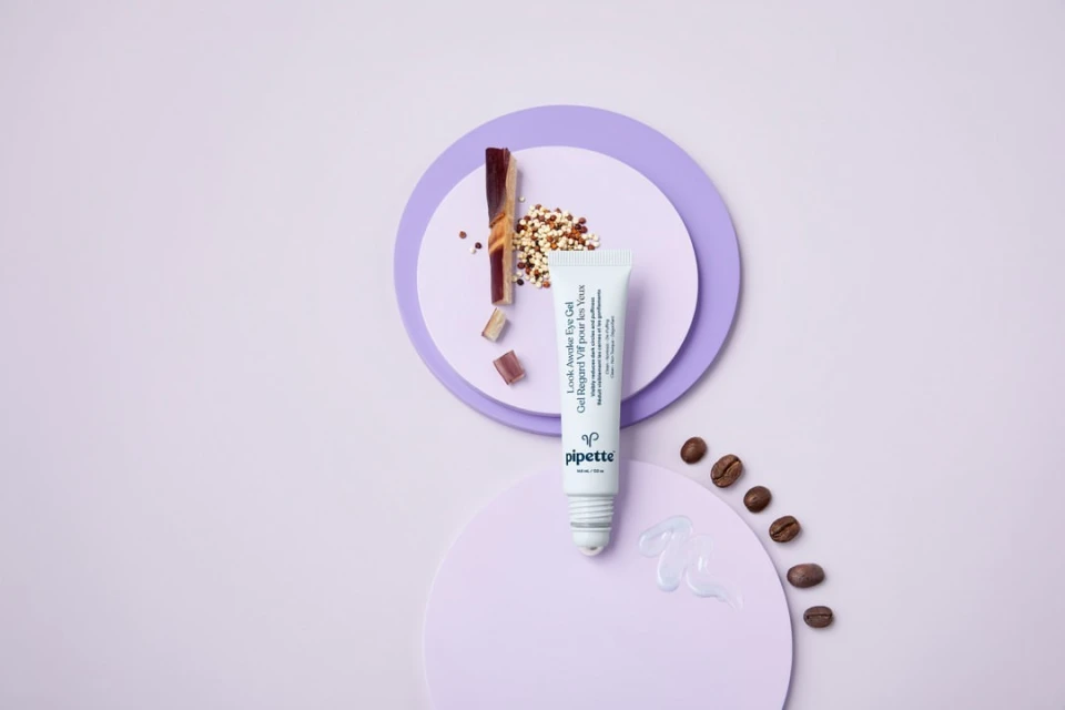 Eye gel tube by Pipette, brown coffee beans, and geometric lavender shapes on a pale lavender backdrop in studio product shot.