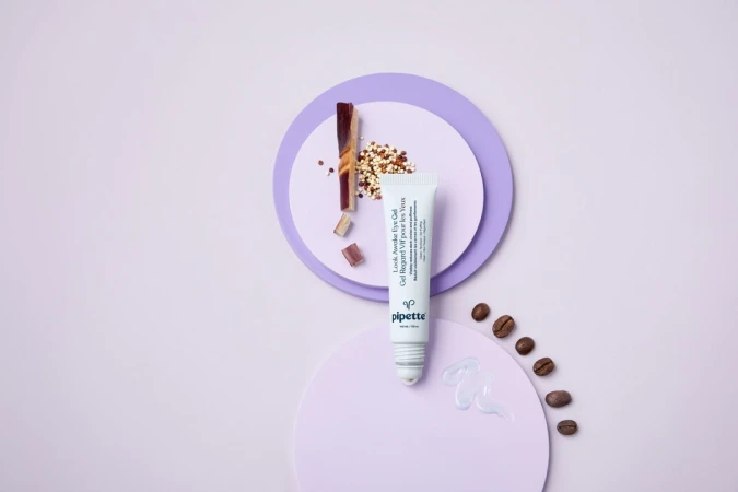 Eye gel tube by Pipette, brown coffee beans, and geometric lavender shapes on a pale lavender backdrop in studio product shot.