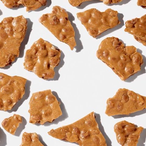 Overhead shot of peanut brittle pieces with light tan and golden brown colors, scattered on a plain white surface in a flat lay.