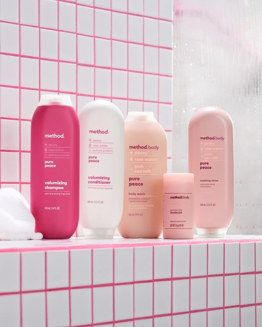Method brand bath and body products on a pink tiled shelf including shampoo, conditioner, body wash and deodorant in pink and white bottles.