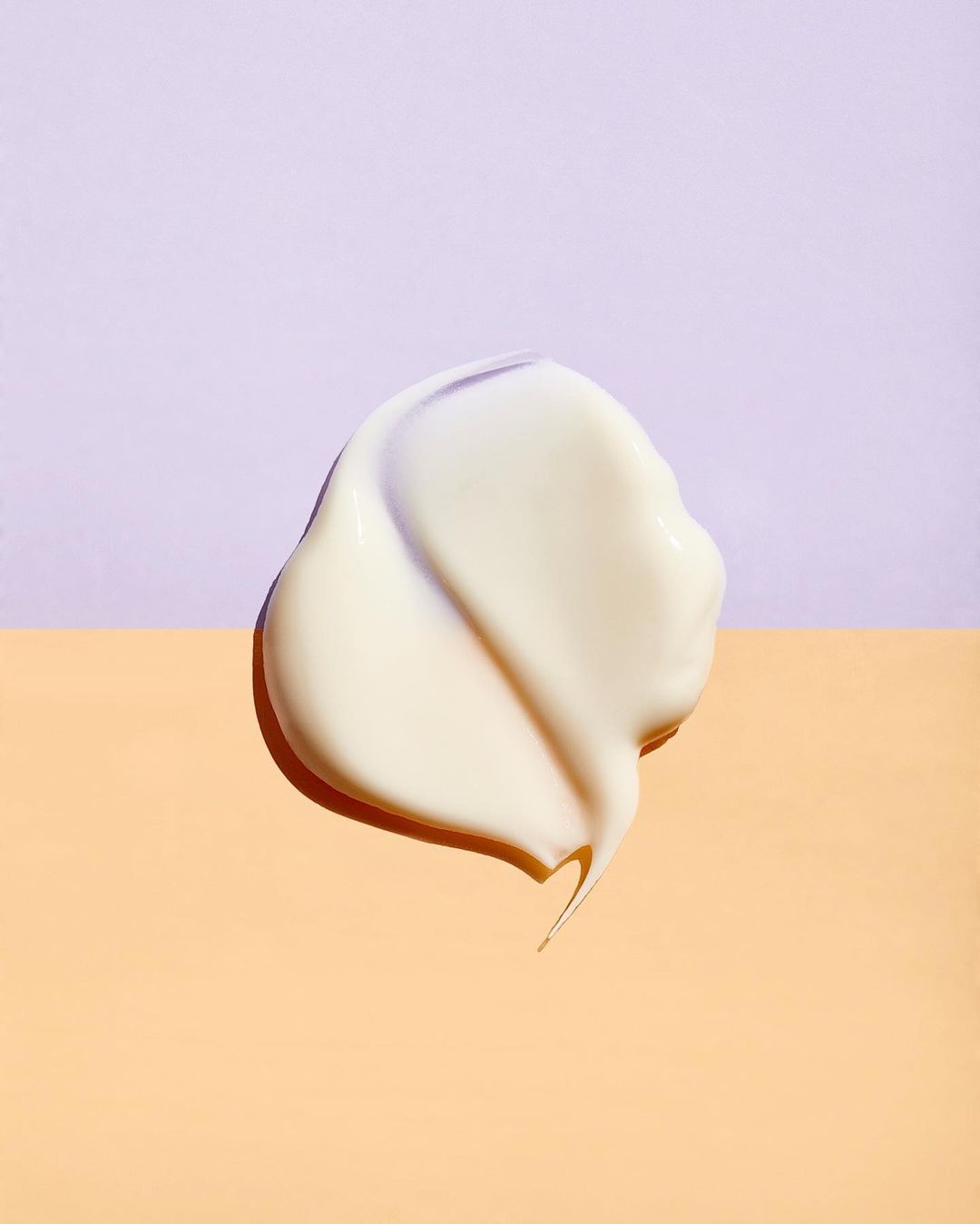 Creamy cosmetic product swatch on contrasting two-tone backdrop of pastel purple and peach, beauty and skincare concept.