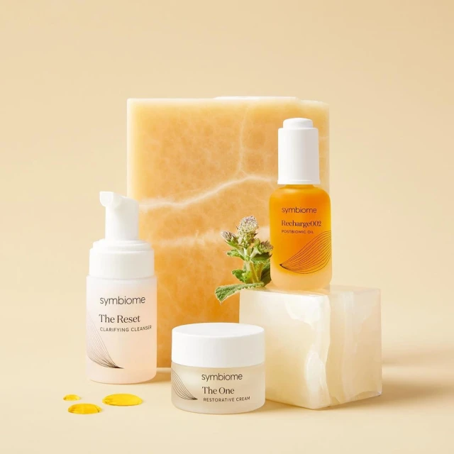 Symbiome skincare product bottles displayed on marble blocks against a light yellow background in a visually appealing product shot.