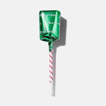 Wrapped See's Candies Mint Cream lollipop with a white and pink striped stick on a white surface, offering a sweet confectionery treat.
