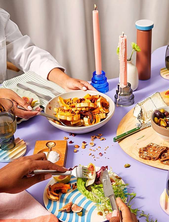 Overhead shot of a lilac table featuring two diners enjoying a meal with salads, figs, cheese, crackers, and lit candles for ambiance.