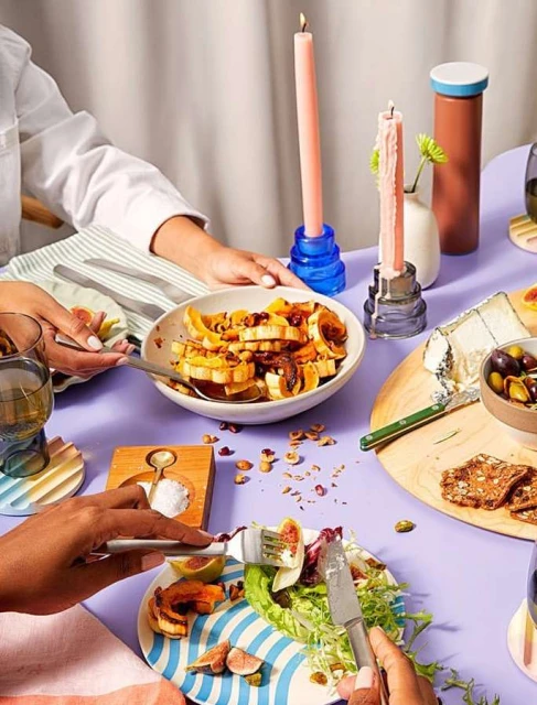 Overhead shot of a lilac table featuring two diners enjoying a meal with salads, figs, cheese, crackers, and lit candles for ambiance.