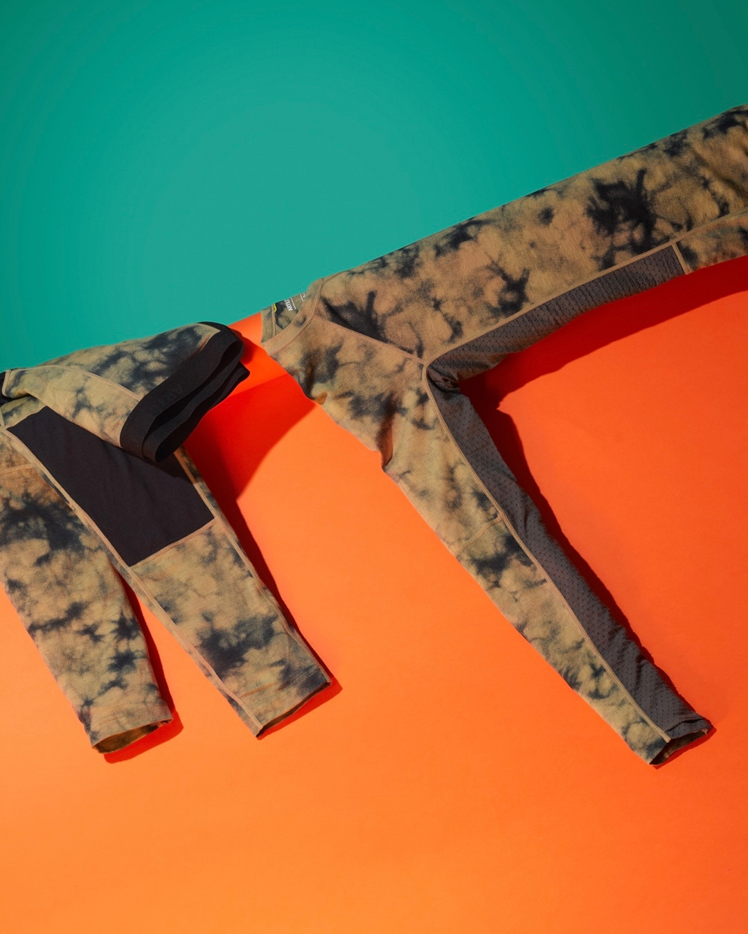 Two patterned athletic leggings, one folded, placed diagonally across an orange and teal background creating a color block effect.