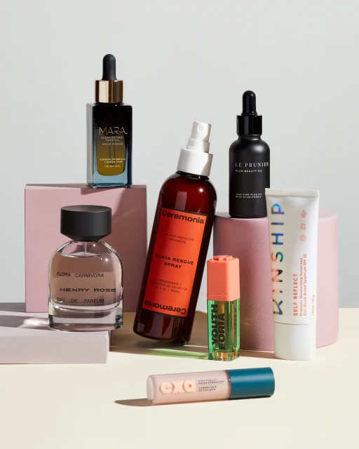 Multiple beauty and skincare products arranged on pastel platforms: perfume, serum, spray, lotion, and cream containers against a white backdrop.