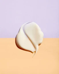 A smooth white cream swatch centered on a split-color background of pale purple and soft peach.
