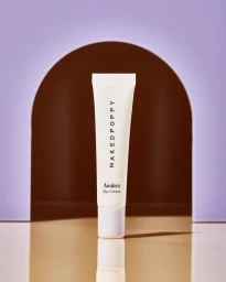White skincare tube with black lettering standing upright on a reflective surface in front of a dark brown arch and purple background.