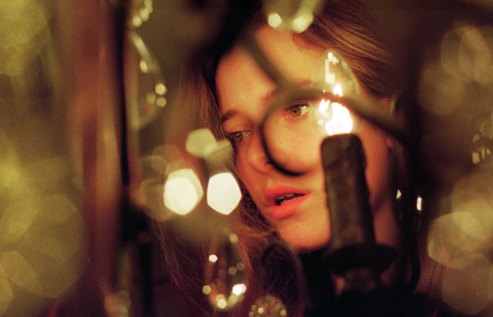 Close-up of a woman with light brown hair looking downward, illuminated by the warm glow of candlelight with bokeh effects.