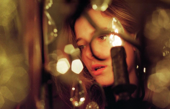 Close-up of a woman with light brown hair looking downward, illuminated by the warm glow of candlelight with bokeh effects.