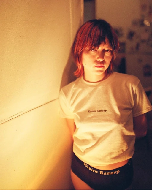 Portrait of a young adult female indoors, wearing a branded white tee-shirt and black underwear with the brand name visible.