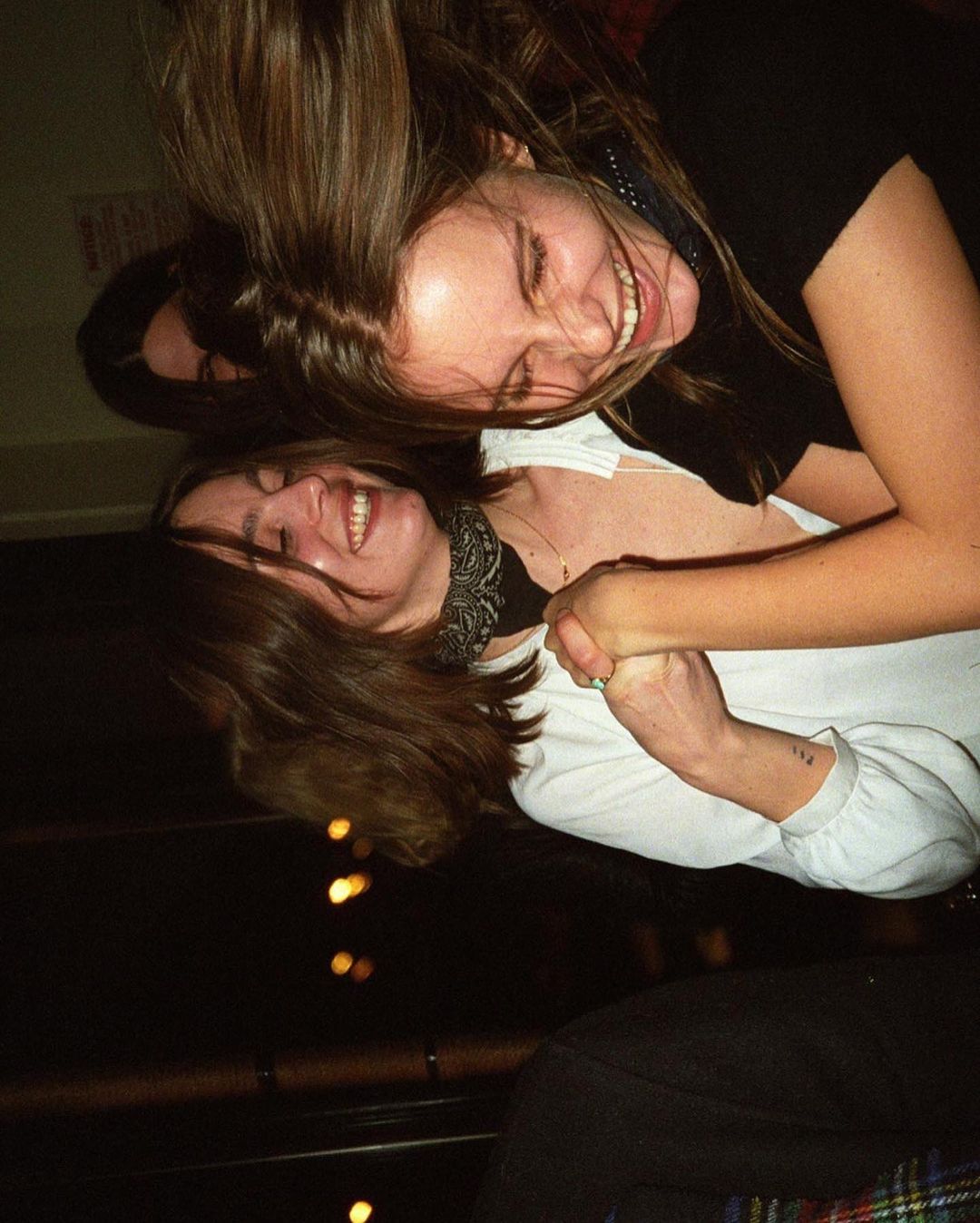 Two adult females laughing and embracing in a dimly lit indoor environment, capturing a candid moment of joy and camaraderie.