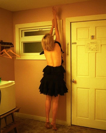 Woman in black tiered ruffled dress standing on tiptoes with arms raised inside a warm-lit room
