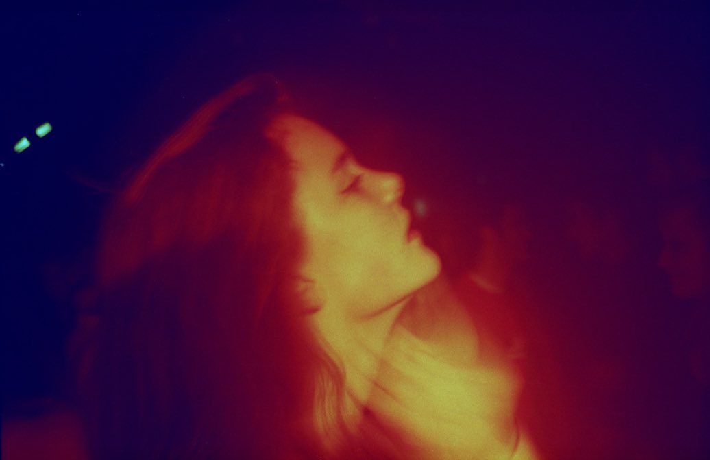 Close-up profile shot of a woman with long hair looking up, bathed in reddish-yellow light against a dark purple background.