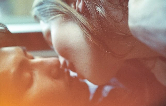 Close-up portrait of a couple with light skin tones kissing in soft, diffused lighting, captured with a shallow depth of field.