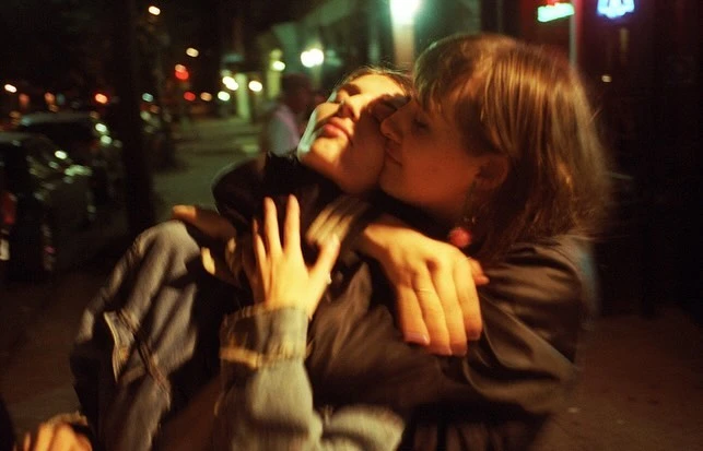 A photo captures a couple embracing on a city street at night, under the glow of streetlights, with blurred bokeh adding to the scene's intimacy.