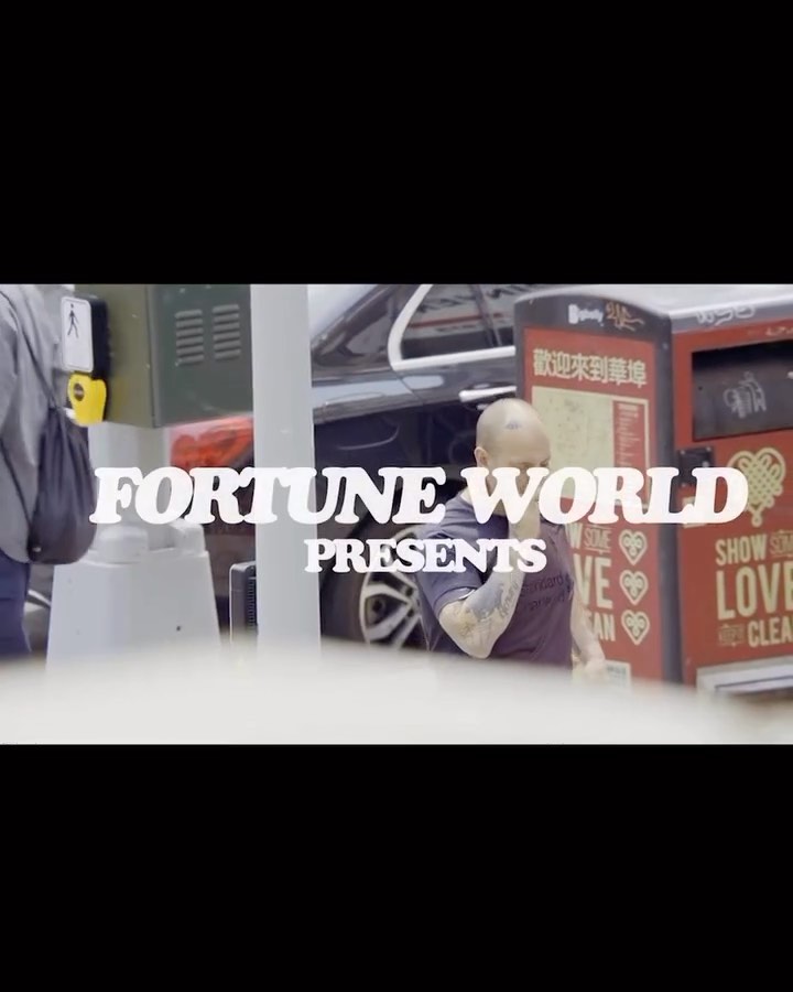 Man with tattoos stands near a bus stop in an urban setting. Foreground text reads 'Fortune World Presents'.