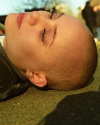 Close-up portrait of a bald woman lying down outdoors with a teardrop on her cheek, captured by Chad Moore in New York.