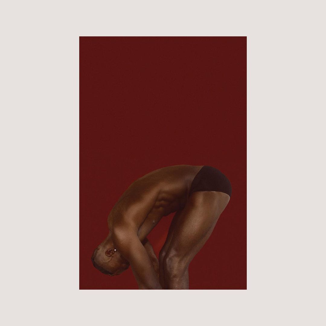 Male figure in a bent-over pose against a red background, creating a visually striking and minimalistic composition with studio lighting.