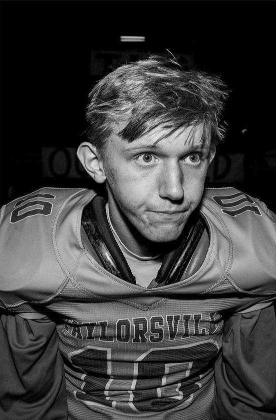 Black and white portrait of a young football player in uniform with 'TAYLORSVILLE' visible, against a dark background.