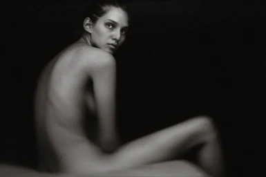 Portrait of a woman sitting in profile looking back over her shoulder against a dark background by Chadwick Tyler