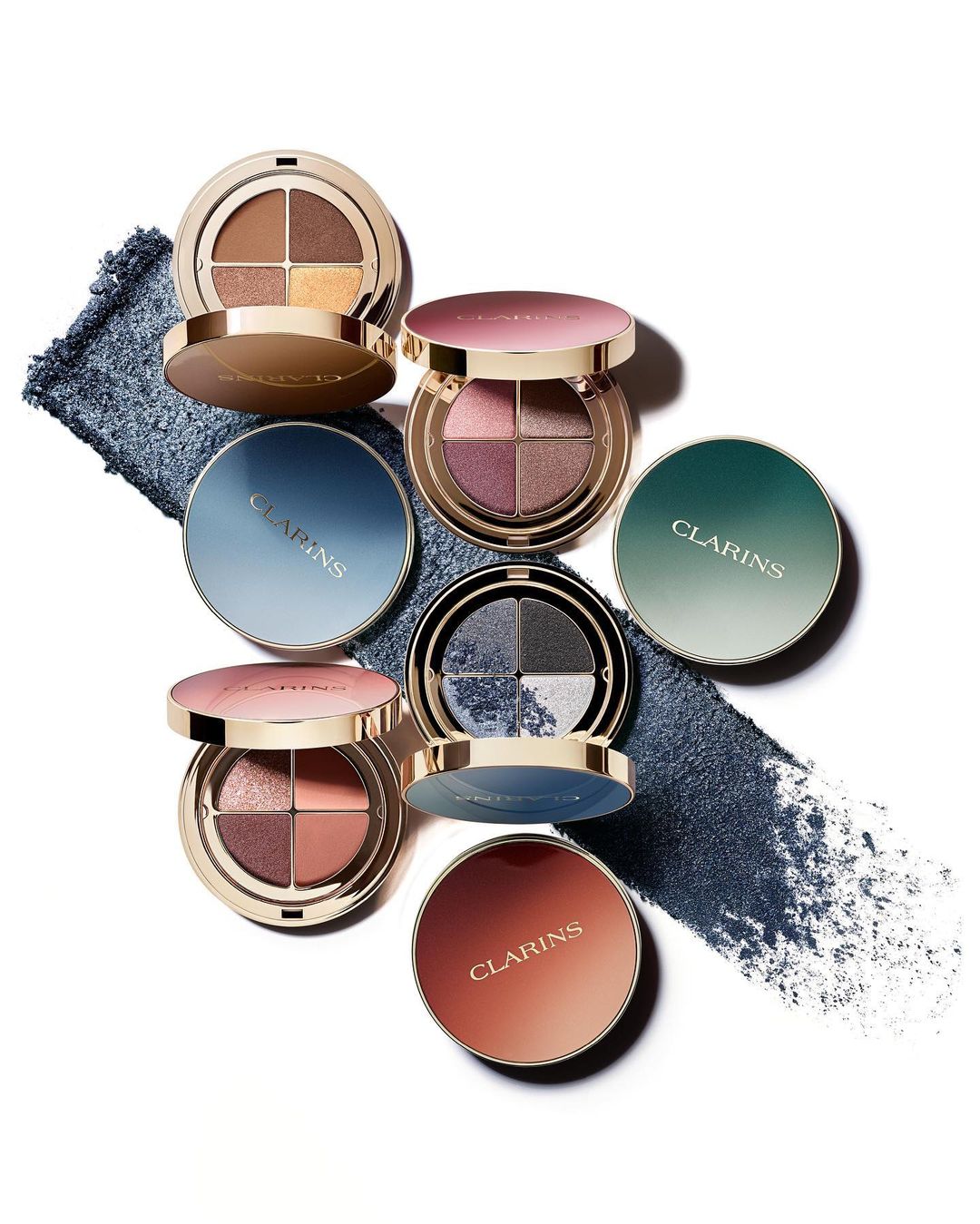Several opened Clarins eye shadow palettes arranged with loose pigment on a white background in a beauty and cosmetic product shot.