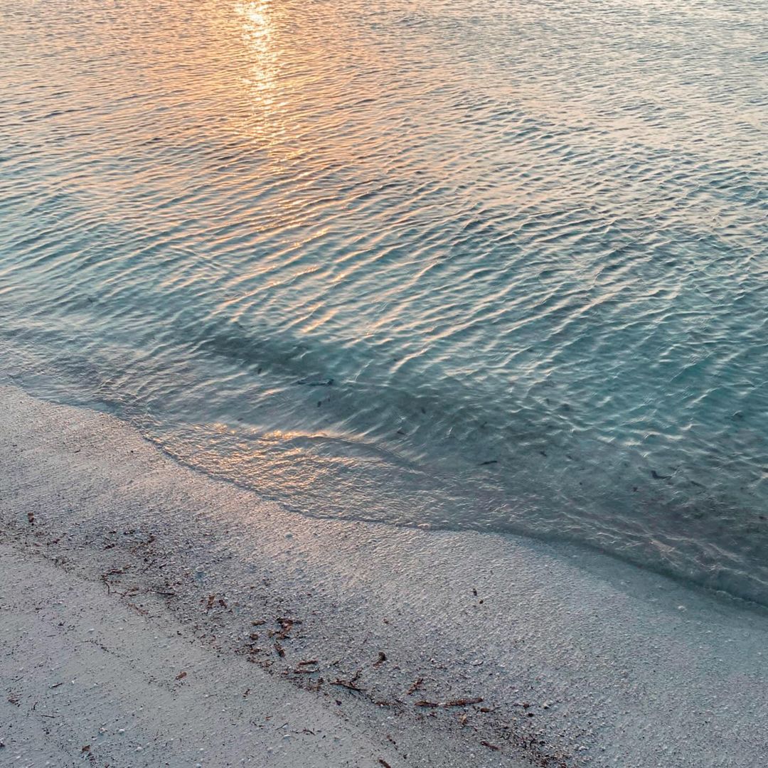 Beach scene with clear turquoise water gently rippling near a sandy shore, bathed in soft, warm sunlight, creating a serene seascape.
