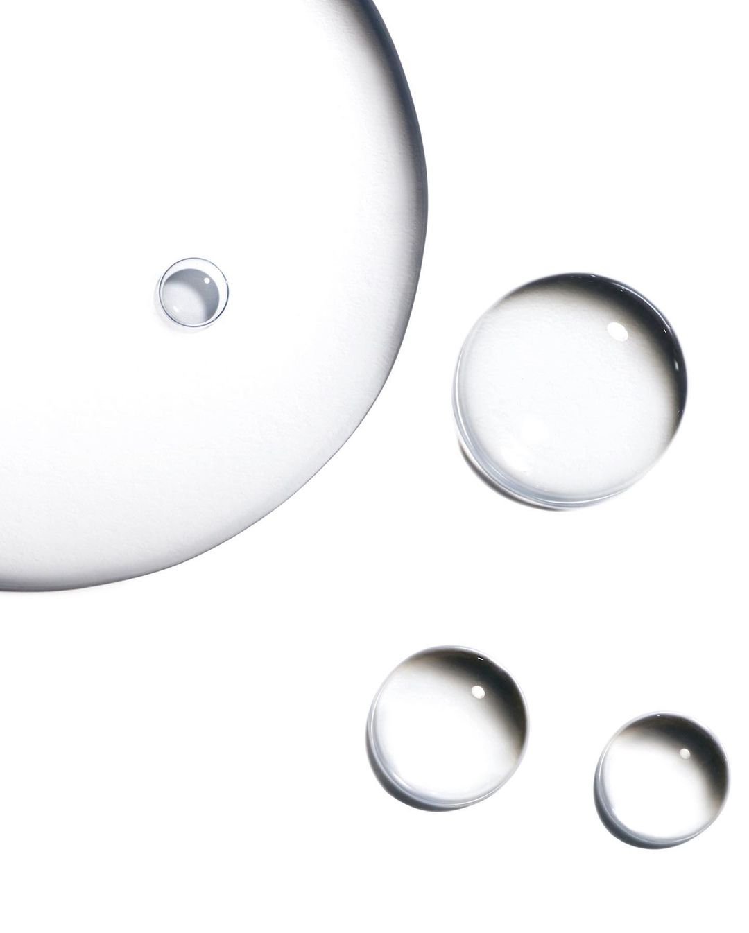 Close-up shot of clear liquid droplets on a white background, showcasing skincare or cosmetic product texture.