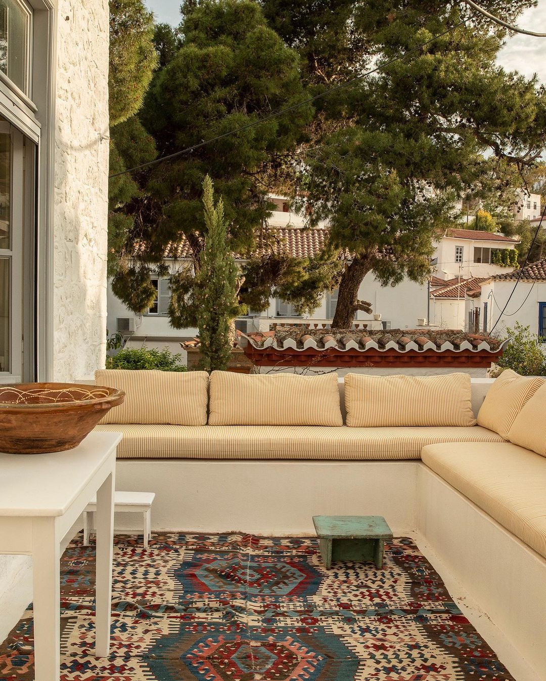 Outdoor patio featuring built-in seating with cushions, a patterned rug, and a small table with a wooden bowl on top.