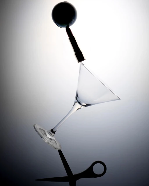 Abstract still life featuring a cocktail glass, lipstick, black sphere, and scissors balanced against a gray gradient background.