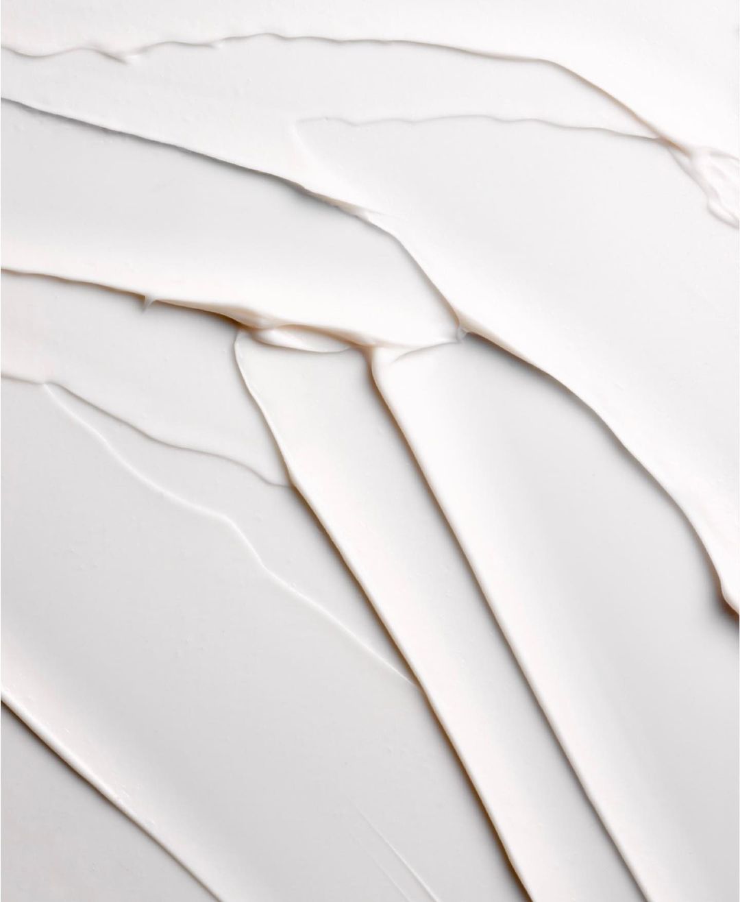 Close-up of thick white cream with textured patterns. Cosmetic product shot highlighting smooth texture and reflective surface.