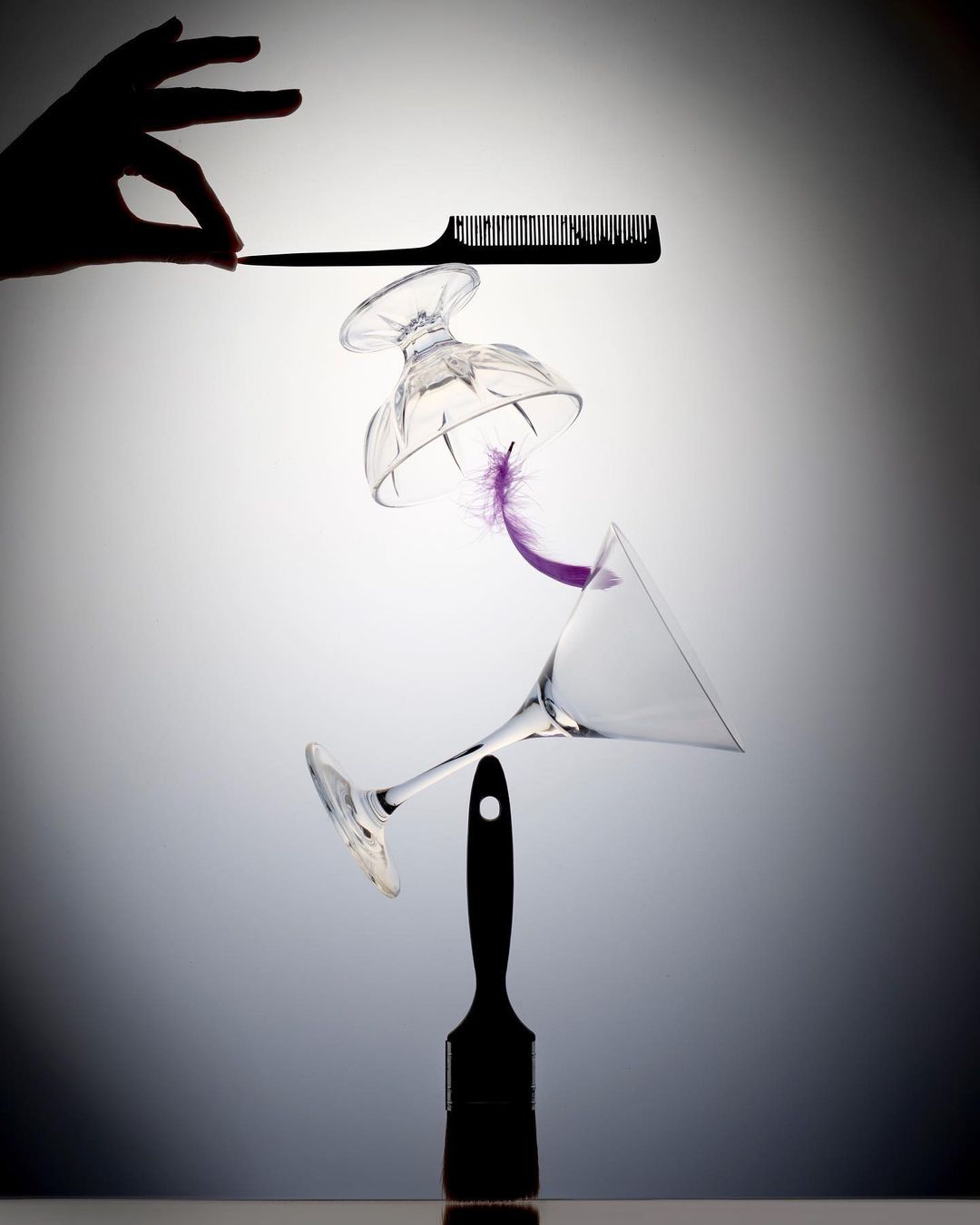 Abstract still life composition featuring a hand, comb, glasses, purple feather, and paintbrush against a gradient background.