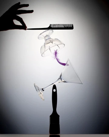 Abstract still life composition featuring a hand, comb, glasses, purple feather, and paintbrush against a gradient background.