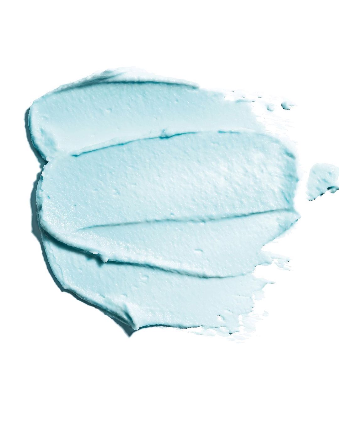 Close-up of a textured swipe of light turquoise cream, possibly cosmetic or skincare product, set against a bright white background.