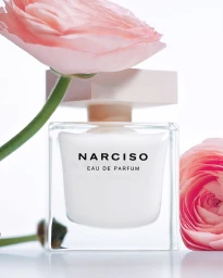 Square perfume bottle with white contents and pink flowers next to it against a seamless white background
