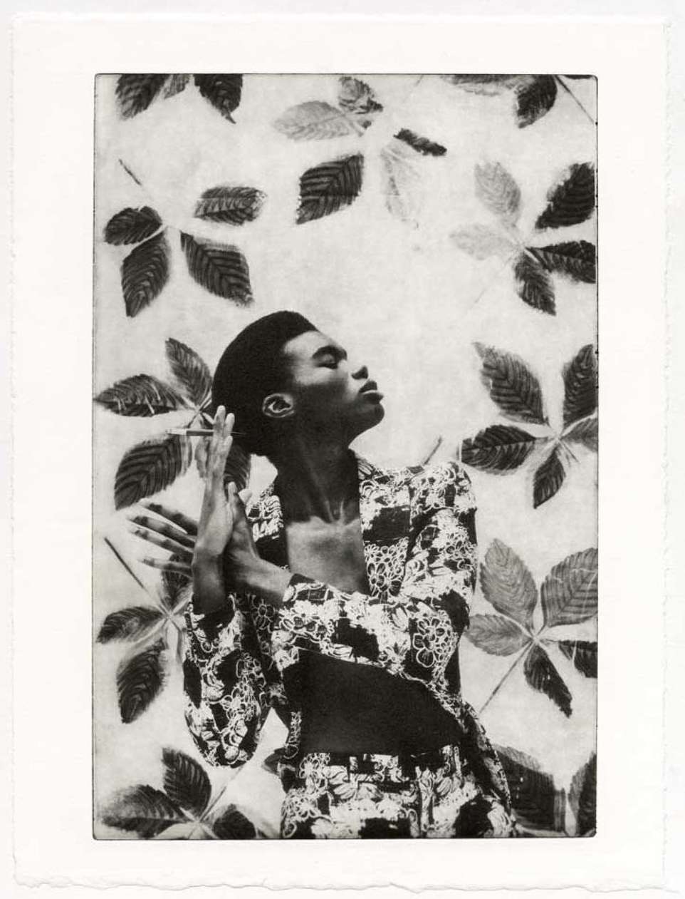 Monochrome art print of a Black model posing in patterned suit, hands clasped in a print with leaf shapes on a textured background.