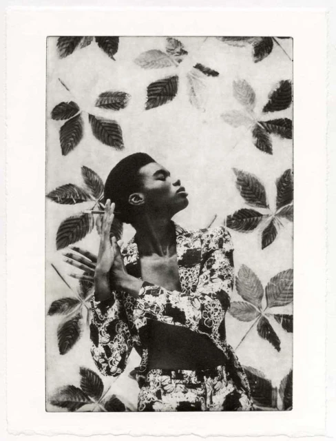 Monochrome art print of a Black model posing in patterned suit, hands clasped in a print with leaf shapes on a textured background.
