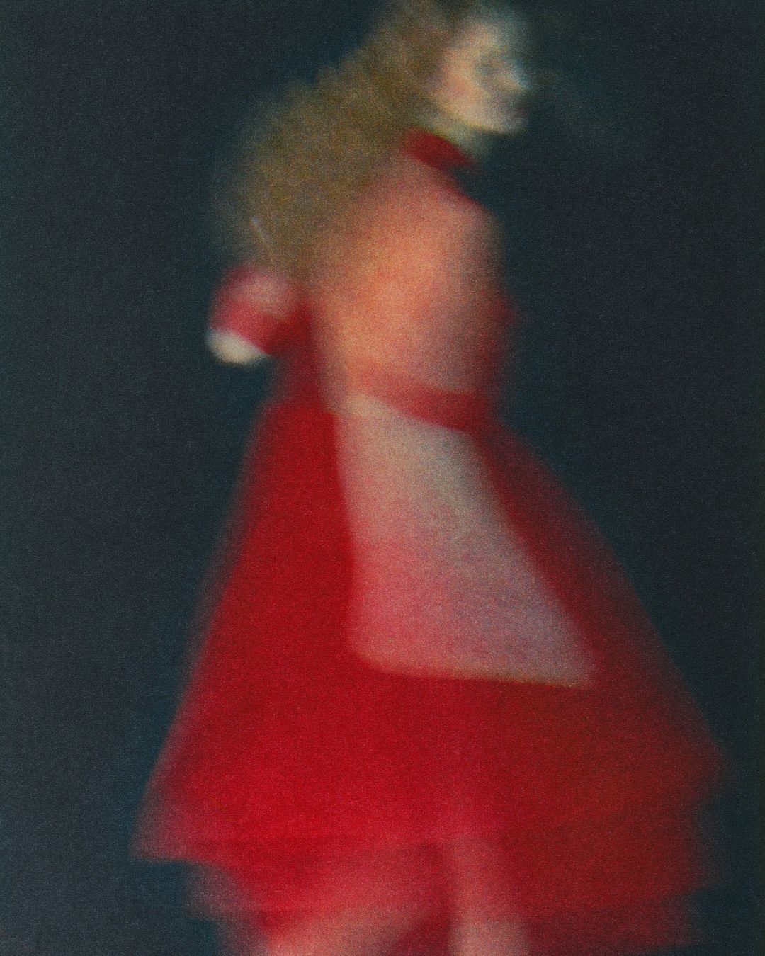 Abstract fashion photograph of a woman in a red dress, with long exposure blur and artistic motion creating a sense of dreamy movement.