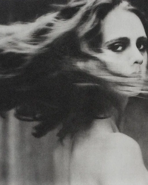 Black and white portrait of a woman with long, wind-blown hair, facing the camera with a neutral expression, wearing a dark choker necklace.