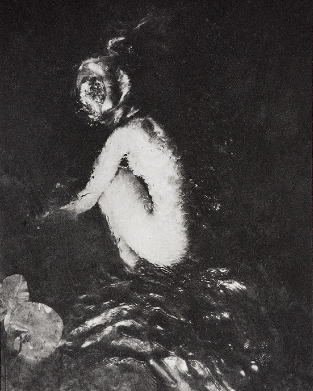 Monochromatic art photograph of an individual in water, depicted in a kneeling position with lily pads in the lower left corner.